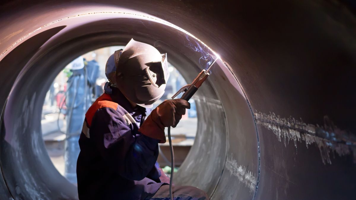 Industrial welder welding two pieces of large pipe together.